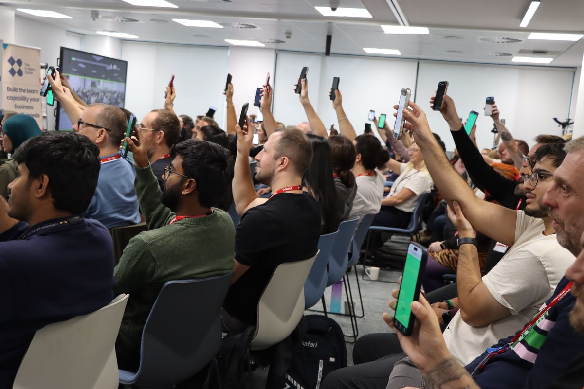 An audience with their phones held above their heads, screens lit, during a pixelmesh effect