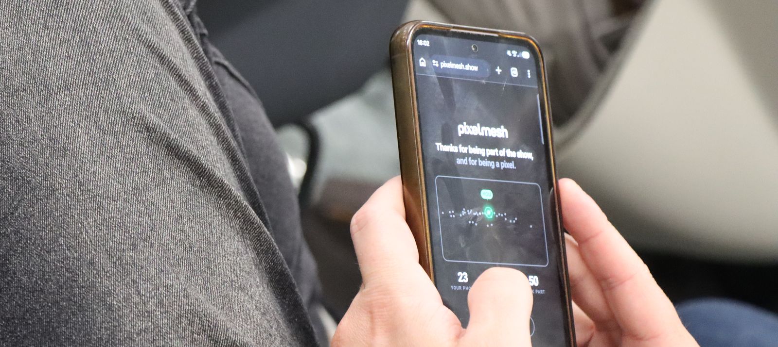 An audience member holding a phone showing the pixelmesh closing card: thanks for being part of the show, and for being a pixel, with their own stats beneath it